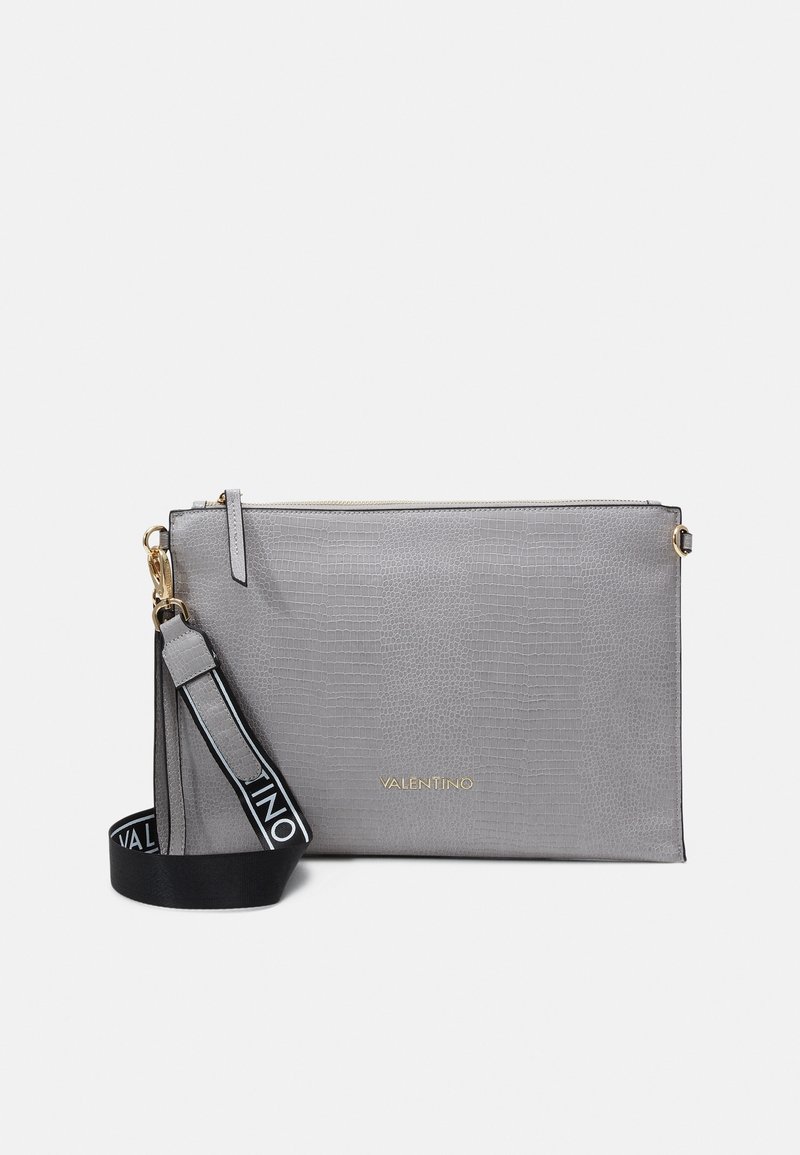 Sac à main en cuir gris avec une finition texturée, doté d'un logo doré et d'une bandoulière noire amovible avec lettrage blanc. Fermeture éclair.