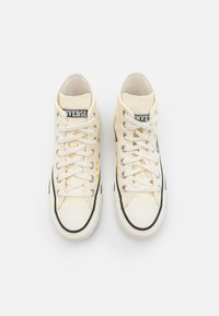 Baskets montantes en toile crème avec des lacets blancs et des semelles en caoutchouc noir. Présente des accents étoilés colorés et un patch logo sur la languette.