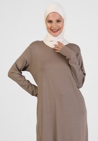 Langärmliges, locker sitzendes Kleid aus weichem braunem Stoff, kombiniert mit einem hellbeigen Hijab. Glatte Textur und entspannte Silhouette.
