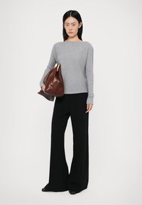 Suéter cinza com nervuras e um decote largo, combinado com calças largas pretas. Segurando uma bolsa de couro castanho com um detalhe em ouro.