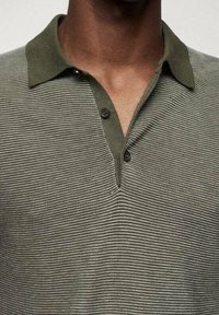 Polo shirt vert olive avec un motif texturé et rayé. Il présente un col rabattu avec deux boutons et des bords de col côtelés.