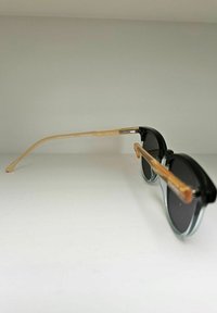 Lunettes de soleil modernes noires avec des verres teintés, une monture transparente bleue et des branches couleur marron clair avec des détails imprimés.