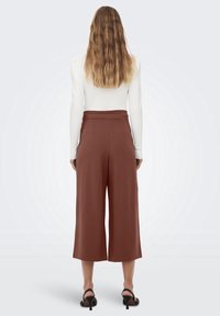 Culottes marron à taille haute, réalisées dans un tissu lisse. Dotées d'un design élégant et d'une coupe large et raccourcie. Talons noirs à brides inclus.