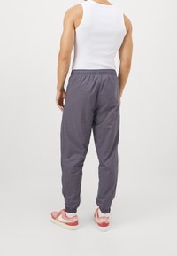 Grå elastiska midjebyxor med avslutade anklar, tillverkade av ett lätt material, i kombination med rosa och vita sneakers.