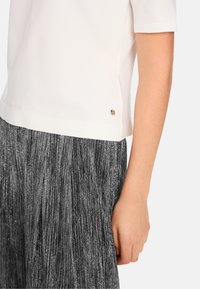 White short-sleeve top with a rounded hem, paired with a black metallic pleated skirt. Notable gold accent detail on the top's side.