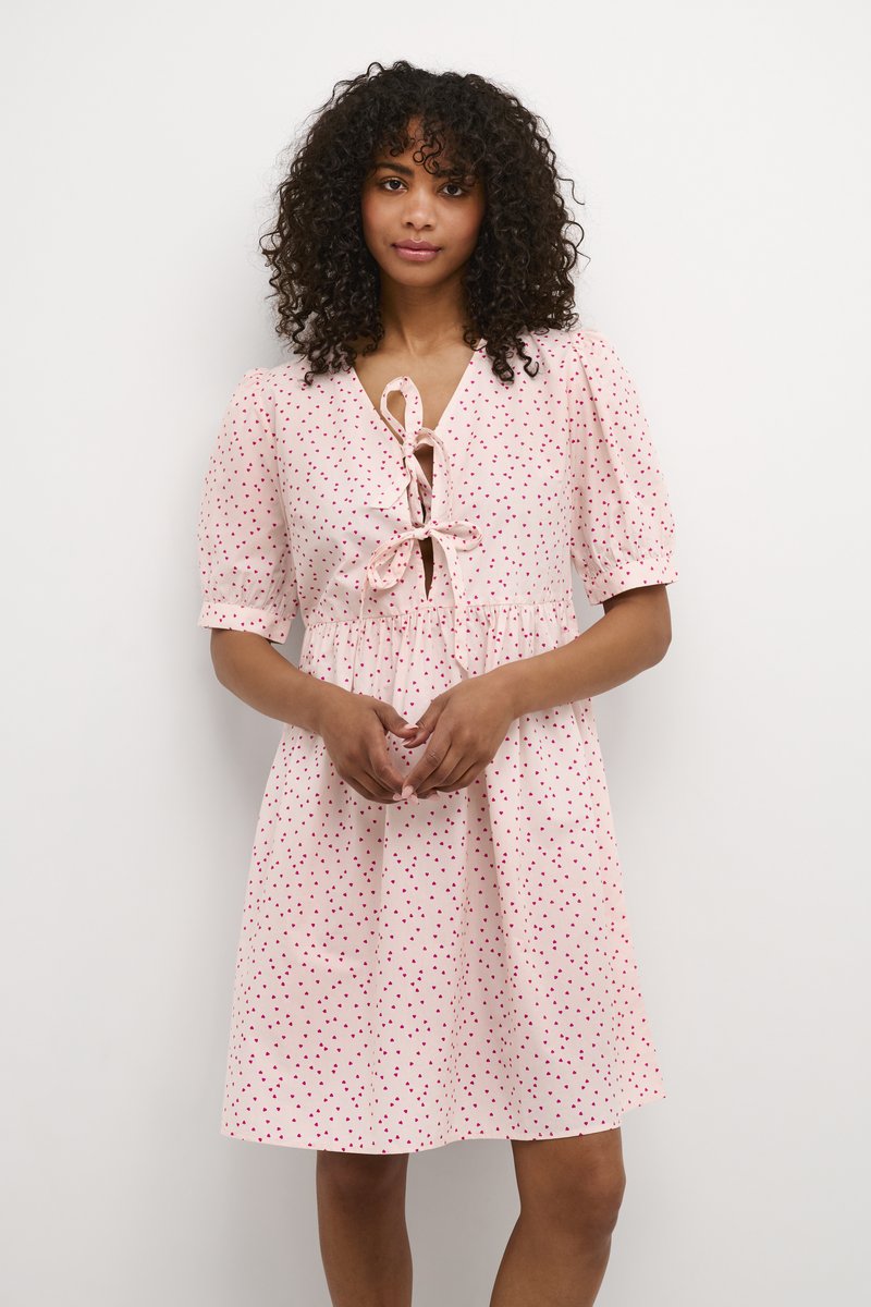 Rosa Kleid mit kurzen Puffärmeln, einem Bindeband vorne und verstreuten roten Punkten. Der Stoff ist leicht und hat eine lockere Passform.
