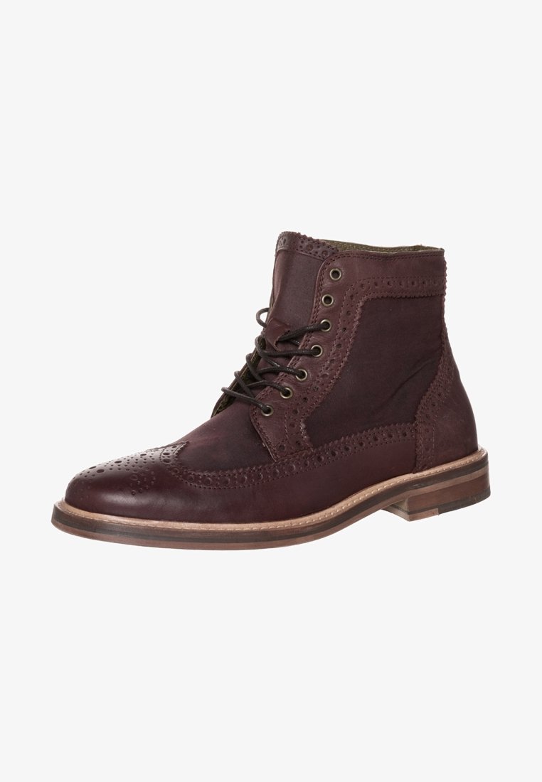 Bottine brogue en cuir marron foncé avec perforations décoratives, laçage à l'avant et semelle en bois superposée.
