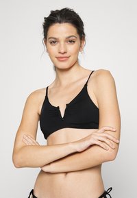 Top de bikini preto com alças ajustáveis, design em V, e detalhe de franzido central, feito de um tecido liso e elástico.