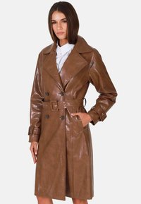 Ruskea nahkainen trench-coat, jossa on kaksirivinen nappilukko, leveät kaulukset, vyö vyötäröllä ja sivutaskut. Sileä, kiiltävä pinta.