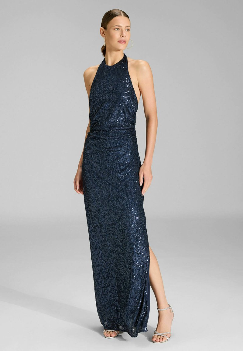 Robe de soirée bleu marine en sequins avec un col licou, un corsage ajusté et une fente latérale, présentant une texture lisse et scintillante. Talons argentés à brides.