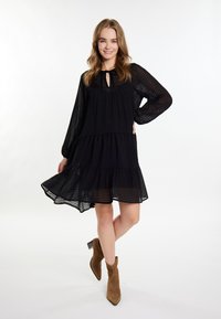 Rochie lungă cu mâneci lungi, cu dungi negre și tiv în straturi, având detalii cu decolteu tip ochi de cheie, asociată cu botine maro până la gleznă. Material ușor și fluid.