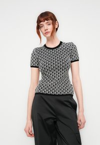 Zwart-witte t-shirt met korte mouwen met een geometrisch patroon, ronde halslijn en ribgebreide manchetten, gecombineerd met zwarte wijde broek.