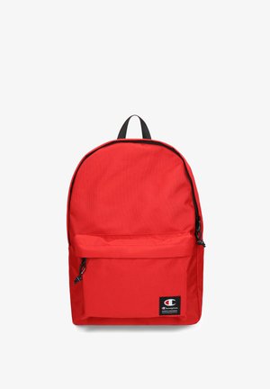 Red fabric backpack with a rounded design, black zipper accents, front pocket, and a logo patch at the bottom right. Adjustable straps included.