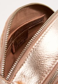 Wnętrze torebki w kolorze różowego złota z metalicznym wykończeniem, gładką fakturą, z zamknięciem na zamek i płaską kieszonką w pasującym odcieniu. Wyłożona brązową tkaniną.