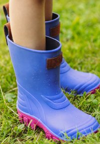Blaue Gummistiefel mit einem strukturierten Design, braunem Klettverschluss und pinken, gerippten Sohlen. Wassertropfen sind auf der Oberfläche sichtbar.