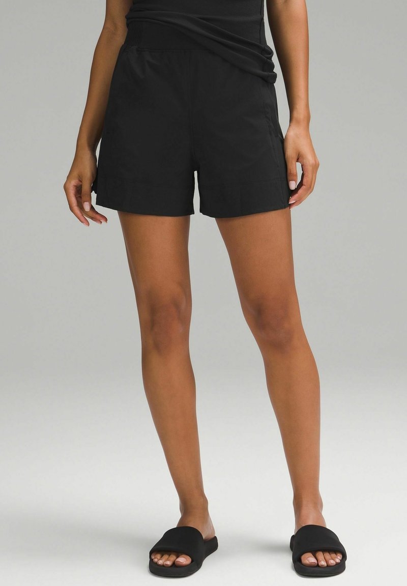 Schwarze Sportshorts mit entspannter Passform, ausgestattet mit einem elastischen Bund und seitlichen Taschen. Glatter Stoff, Länge bis über das Knie.