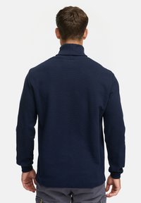 Pull bleu marine à col haut, à texture côtelée et à manches longues. Conçu pour une coupe ajustée avec une finition lisse.
