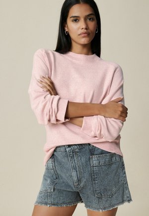 Light pink knit sweater with a crew neck and rolled sleeves, paired with high-waisted, frayed hem denim shorts in a faded blue tone.