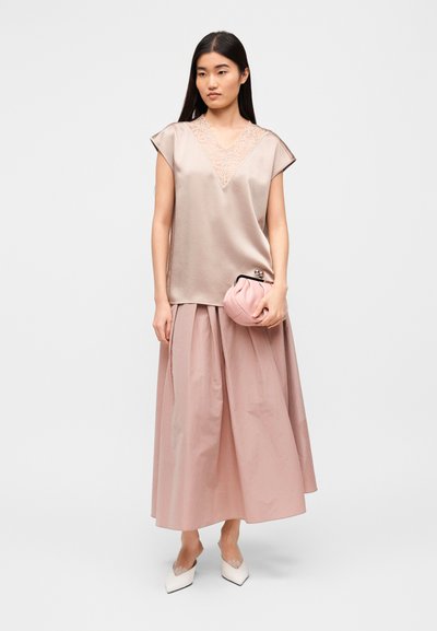 Ροζ σατέν τοπ με λεπτομέρειες δαντέλας, σε συνδυασμό με μια ογκώδη φούστα σε ίδιο χρώμα. Το μοντέλο κρατά ένα μικρό ροζ τσαντάκι και φορεί λευκά μυτερά παπούτσια.