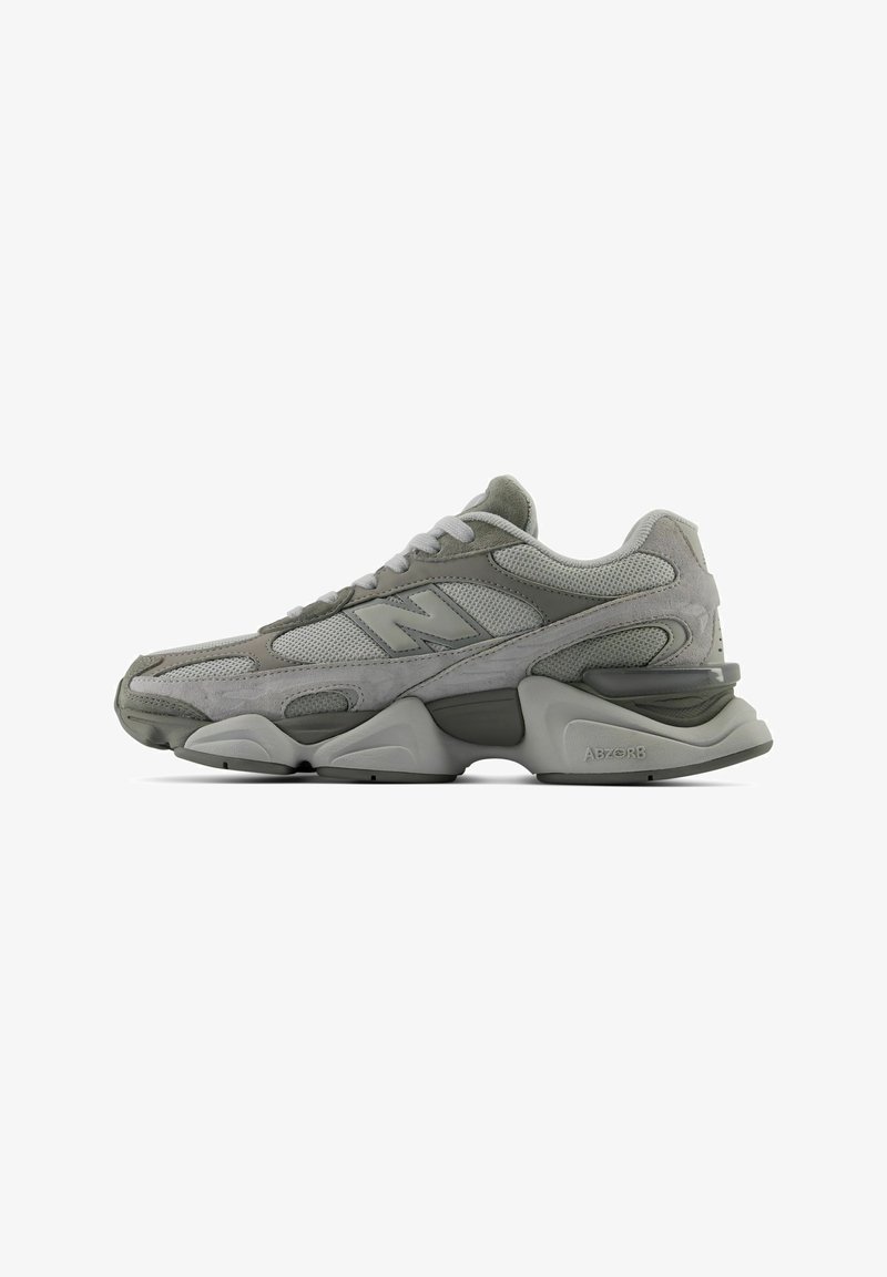 Γκρι αθλητικό παπούτσι New Balance με λεπτομέρειες από διχτυωτό ύφασμα και σουέντ, χοντρή υφασμάτινη σόλα και σχέδιο με κορδόνια, εμφανίζεται από το πλάι σε λευκό φόντο.