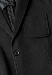 Černý blazer s texturovanou tkaninou, s klopovým límcem, jednokulatým zapínáním a náprsní kapsou na levém prsu.