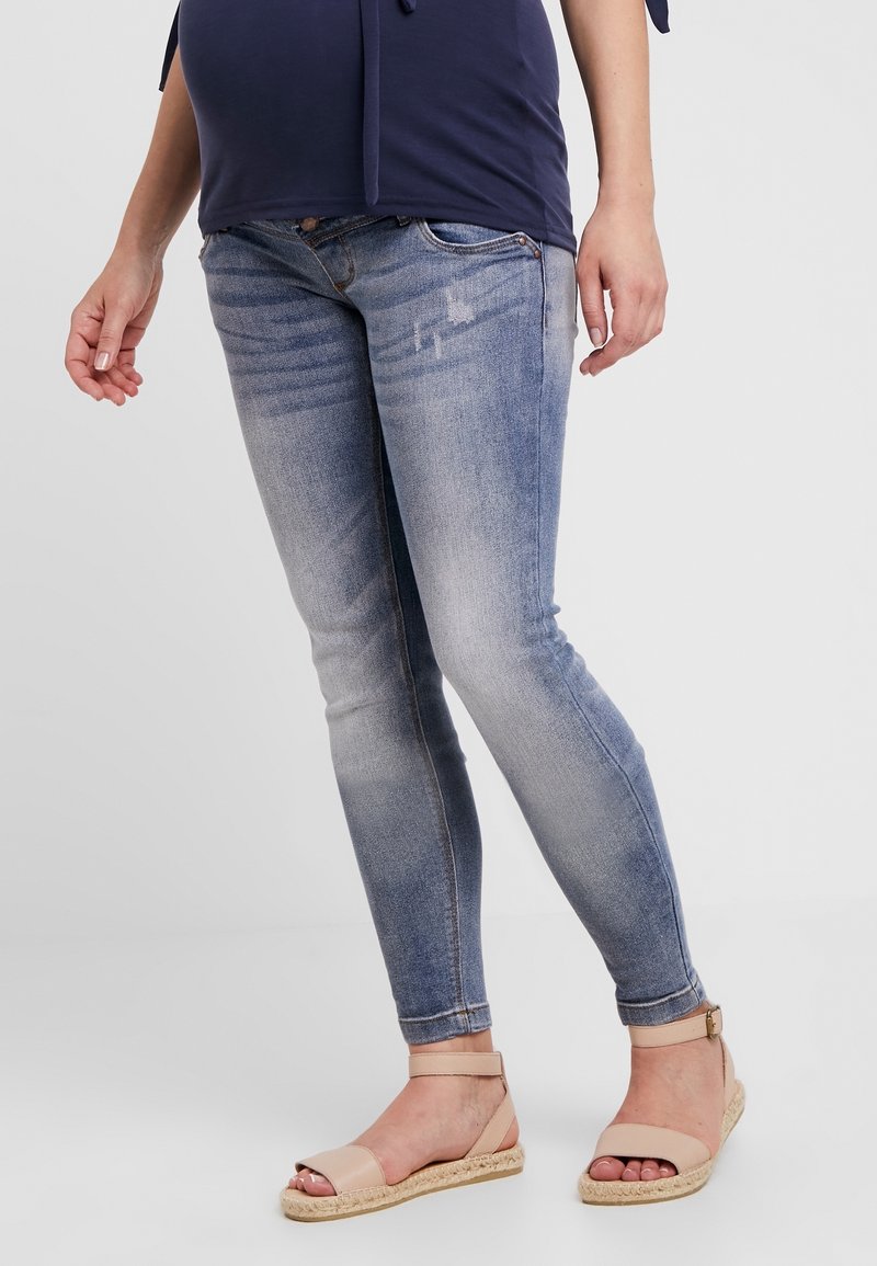 Ljusblå skinny jeans med urtvättning och subtil slitage, parat med beige ankelremssandaletter. Textur av bomullsdenim, tapered fit.