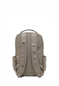 Mochila beige con tirantes ajustables acolchados, bolsillos laterales, asa superior y el logo de Crocs en una de las correas, vista desde la parte posterior.