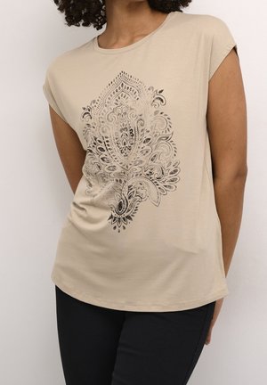 Haut beige à manches courtes avec un grand motif noir paisley complexe, porté avec un pantalon noir, tête du mannequin recadrée.