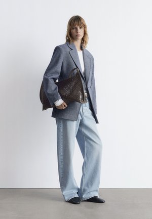 Oversized gray wool blazer, white shirt, baggy light blue jeans, black pointed shoes, and a dark brown woven handbag with a handle.