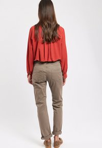 Blouse rouillée raccourcie avec des plis, associée à un chino beige retroussé aux chevilles et des mocassins en cuir l éopard marron. Texture de tissu lisse.