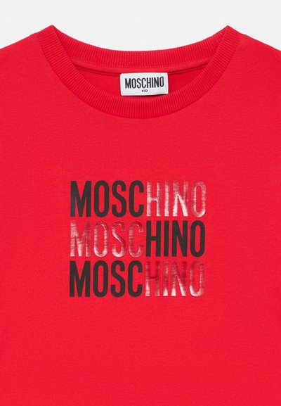 Κόκκινο βαμβακερό t-shirt με το κείμενο "MOSCHINO" σε μαύρο και ασημί, τοποθετημένο κάθετα στην μπροστινή πλευρά. Κλασικός σχ εδιασμός με στρογγυλή λαιμόκοψη.