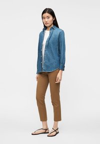 Sinine teksapluus, kantud valge t-särgi peal, pruunide kitsaste pükstega ja mustade sandaalidega. Lihtne ja vabaaja stiil.