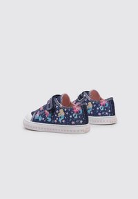 Zapatos de denim azul con patrones de unicornios y flores, cierre de Velcro, suela de goma blanca y acentos en forma de corazón rosa en la base.