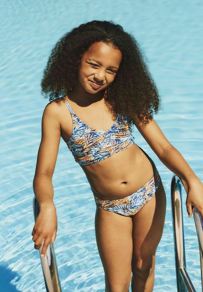 Maillot de bain deux pièces avec un motif de feuilles de palmier vibrant en bleu, orange et jaune. Le haut a des bretelles fines et un décolleté arrondi.