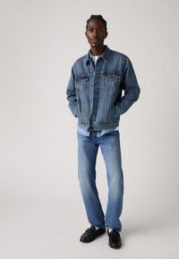 Leren spijkerjack in lichtblauw met een klassiek ontwerp, twee borstzakken en knoopsluitingen, gecombineerd met lichtblauwe jeans en zwarte schoenen.