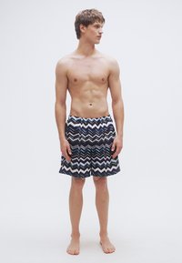 Μαγιό σορτς με ζιγκ-ζαγκ σχέδιο σε σκούρο μπλε, ανοιχτό μπλε και λευκό, με ελαστική μέση και άνετη εφαρμογή.