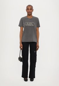 Camiseta de algodón gris con logo de strass, combinada con pantalones cargo negros con bolsillos. Llevada con zapatos negros con tachuelas y un bolso pequeño.