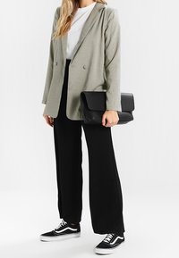 Szara marynarka w jodełkę, czarne spodnie o szerokich nogawkach, biały t-shirt, czarna kopertówka oraz czarne trampki z białymi akcentami. Prosty, dopasowany krój.