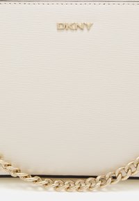 Vit strukturerad läderhandväska med ett guld kedjesnöre och präglad DKNY-logotyp. Minimalistisk design med rena linjer och en kompakt form.