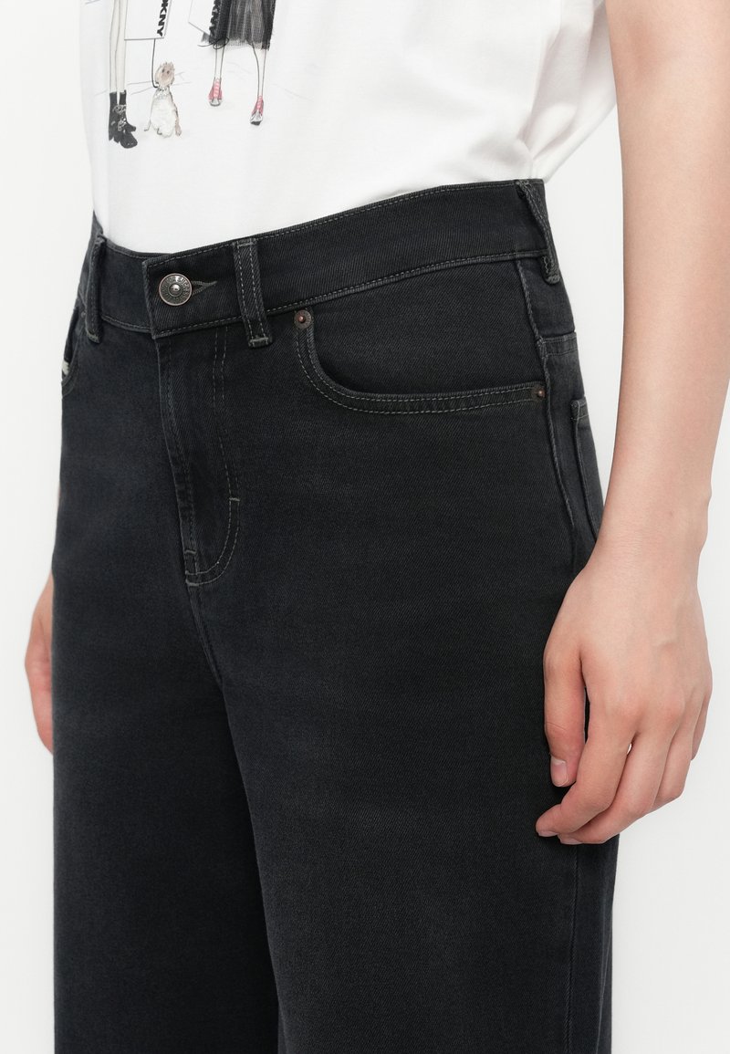 Jean en denim noir à taille haute, avec des détails de couture subtils et des poches avant. Confectionné dans un tissu résistant, avec un système de fermeture à bouton.