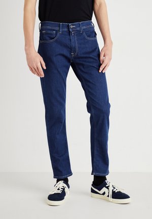 Marinblå denimjeans med slim fit, synlig sömnad, fram- och bakfickor, bärs med svarta strumpor och blå sneakers.