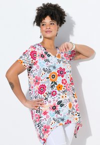 Túnica floral con escote en V en blanco, que presenta un estampado multicolor de flores y hojas. Manga corta y un dobladillo asimétrico.