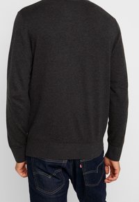 Maglione grigio scuro con maniche lunghe, polsini e orlo a costine; texture liscia, scollatura tonda, indossato su jeans blu.