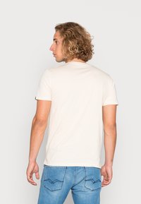 Lys beige kortærmet t-shirt med rund halsudskæring og en blød tekstur, parret med blå jeans med synlige baglommer og syninger.