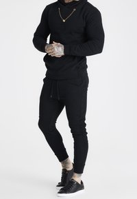 Completo con felpa con cappuccio nera e pantaloni jogger realizzati in tessuto morbido. Presenta una finitura testurizzata, cappuccio con coulisse e dettagli con logo. Abbinato a sneaker nere.