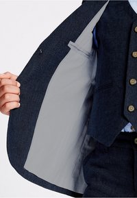 Granatowa kamizelka w garniturze z teksturowanej tkaniny, z szarym podbiciem, wieloma brązowymi guzikami oraz kieszenią po wewnętrznej lewej stronie.