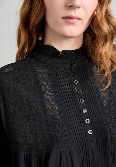 Zwarte blouse met rimpel-kraag, geplooide voorkant, panelen met bloemborduursels en knoopsluiting, die een gestructureerde stof en fijne details toont.