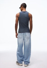 Grijze katoenen tanktop gecombineerd met lichtblauwe wijde spijkerbroeken. De jeans hebben een vervaagde textuur en twee achterzakken.