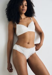 White lace bra with scalloped edges and soft cups, paired with matching lace-trimmed panties. Textured fabric with a delicate appearance.