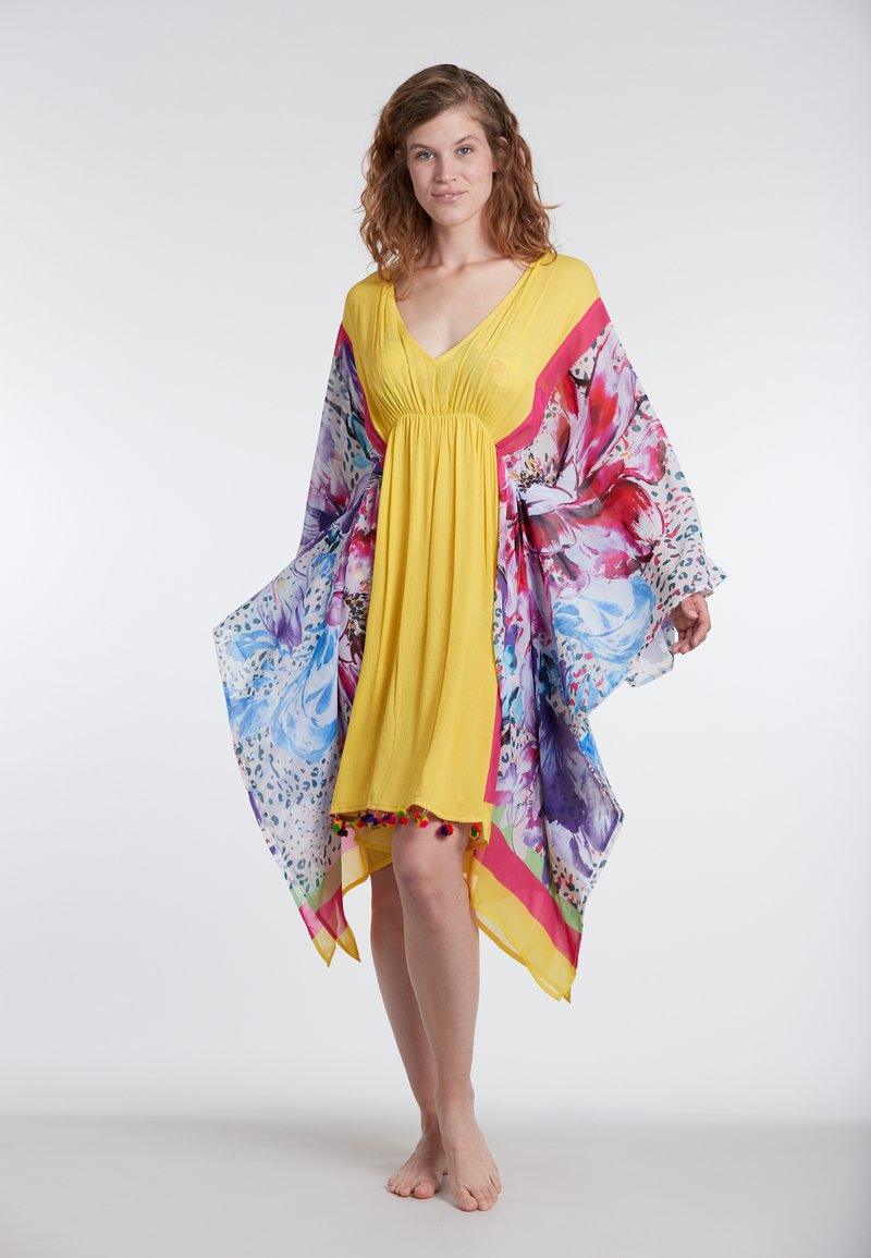 Yellow dress with colorful floral printed cape sleeves, featuring pom-pom trim at the hem. Lightweight, flowing fabric with a V-neck design.